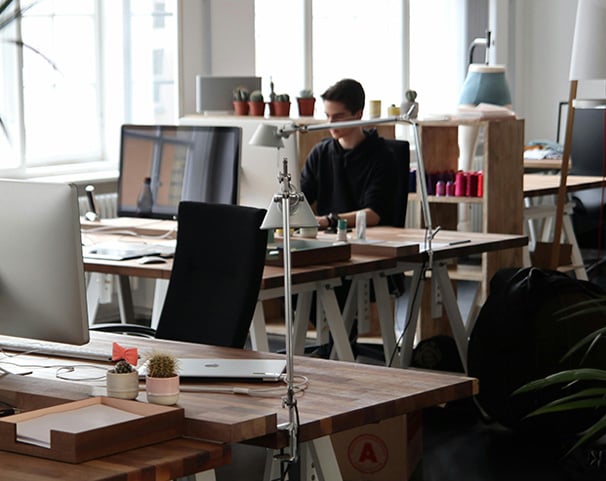 A desk with documents and laptop in a dimly lit room with architectural posters on the wall.