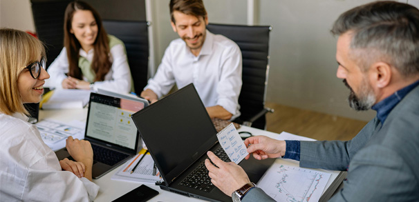 A group of professionally dressed men and women sitting at a conference table with notes and laptops.