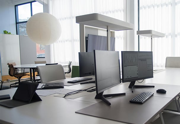 An office workspace with a large table for a shared workspace, with computer keyboards and screens positioned near chairs.