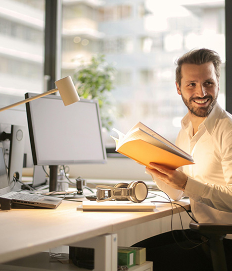 A desk with documents and laptop in a dimly lit room with architectural posters on the wall.